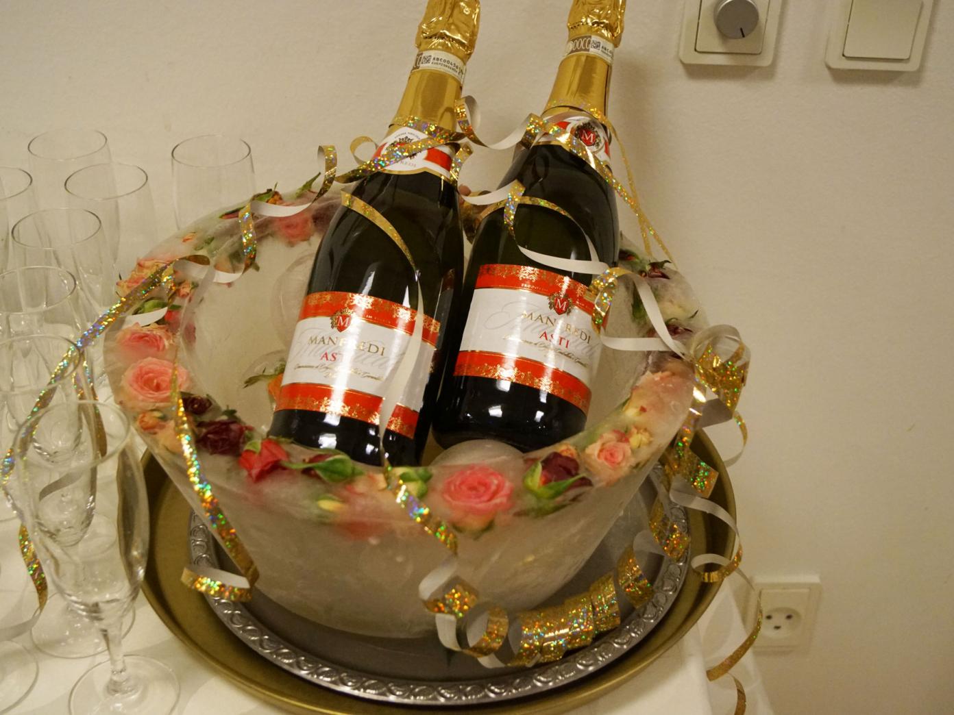 To flasker Asti på køl i en bowle. Flaskerne er pyntet med serpentiner og ved siden af står champagneglas.