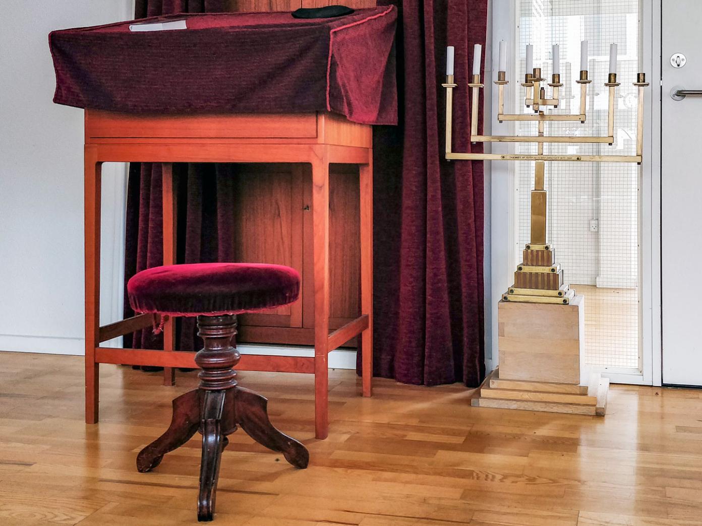 Rum med syvarmet lysestage – menorahen – taburet beklædt med rød velour og jødisk prædikestol med tæppe i rødt velour henover.