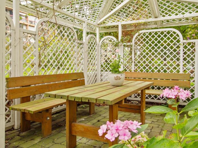 Espalier i hvidt træ med planter kravlende op ad siderne samt et borde- og bænkesæt med en plante i en krukke på bordet.