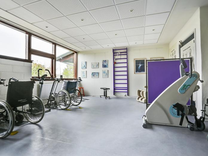 Motionsrum med ribbe, siddende motionscykel og forskellige hjælpemidler. Rummet er lyst med lilla som accentfarve. 