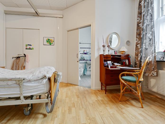 Soveværelse med plejeseng, loftslift og indbygget skab. Soveværelse indeholder også personlige møbler, og fra soveværelset er der adgang til et hvidt klinkebadeværelse.