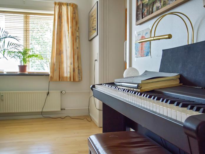 Nærbillede af klaver i lyst rum med billeder på væggene og grønne planter i vindueskarmen.