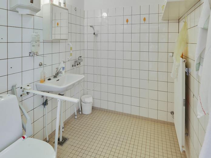 Hvidt flisebadeværelse med toilet, vask, toiletskab og bruser.