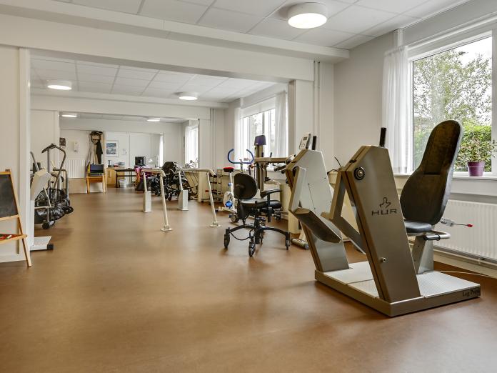 Stort, lyst motionsrum med forskellige træningsmaskiner og gangbarre. 