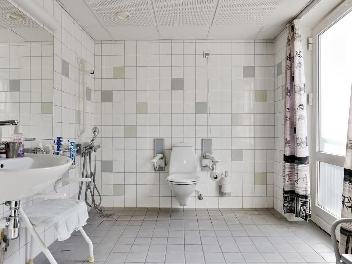 Stort, lyst badeværelse med klinker på gulv og loft samt toilet, vask og stort spejl.