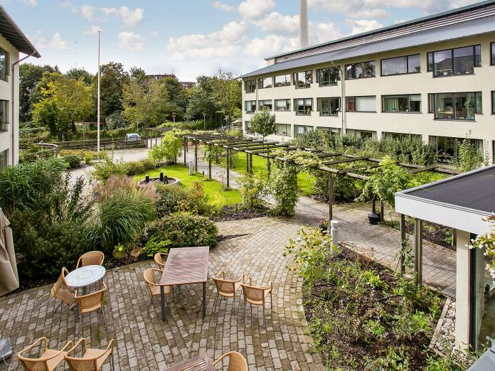 Kig ned på Bispebjerghjemmets have med havemøbler, terrasser, stier og masser af træer, blomster og buske.