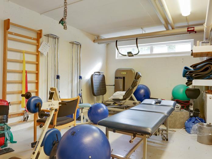Motionsrum i kælderen med maskine, bænk, ribbe, cykel og træningsbolde.