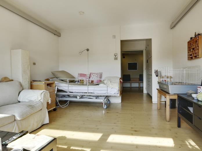 Lyst værelse med seng, loftslift og dør åben ud til gangen samt flere personlige møbler.