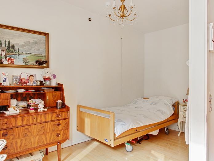 Lyst soveværelse med plejeseng og personlige møbler som et chatol, natbord og en lysekrone.