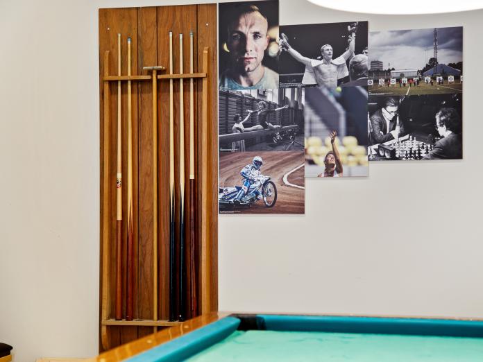 Hjørne af et rum med billardbord, køer på væggen samt billeder af kendte sportsstjerner.