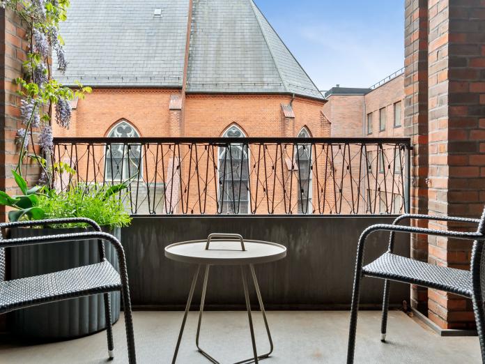 Krog på terrasse med stole, cafébord og grøn klatreplante i krukke. Kig fra terrasse over på en rød murstenskirke i gotisk stil. 