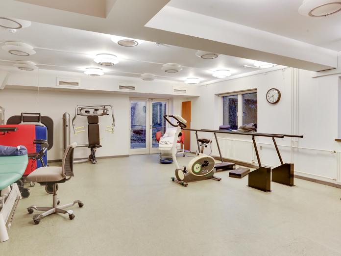 Motionsrum med træningsmaskiner, som fx en kondicykel, samt en gangbarre og en behandlingsbriks.