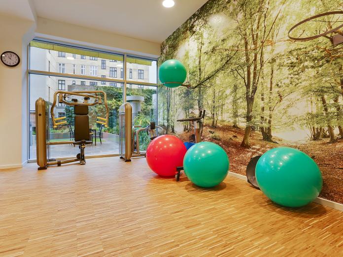 Motionsrum med store vinduespartier ud mod gårdhave samt med den ene væg beklædt med en fotostat af en grøn bøgeskov. Rummet indeholder blandt andet motionsmaskiner og pilatesbolde.