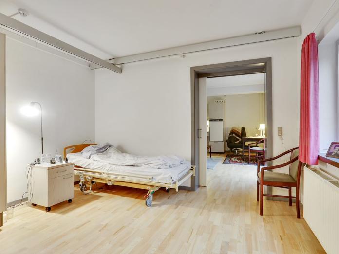 Soveværelse med hospitalsseng, loftslift, indbygget skab og nogle personlige møbler. Der er en skydedør mellem soveværelset og stuen.