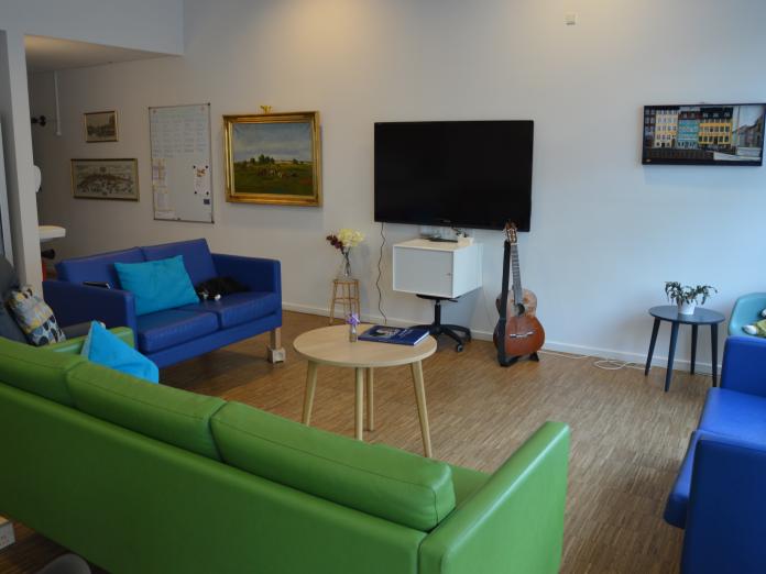 Sofaområde med tre sofaer - to blå og en grøn - tv på væggen, en guitar og et sofabord.
