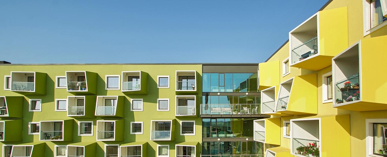Moderne bygning i gule og grøn med altaner og store vinduespartier.